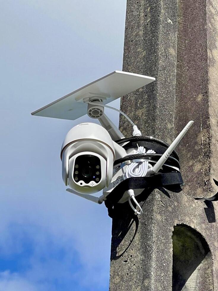 A security camera attached to a pole with a blue sky in the background photo