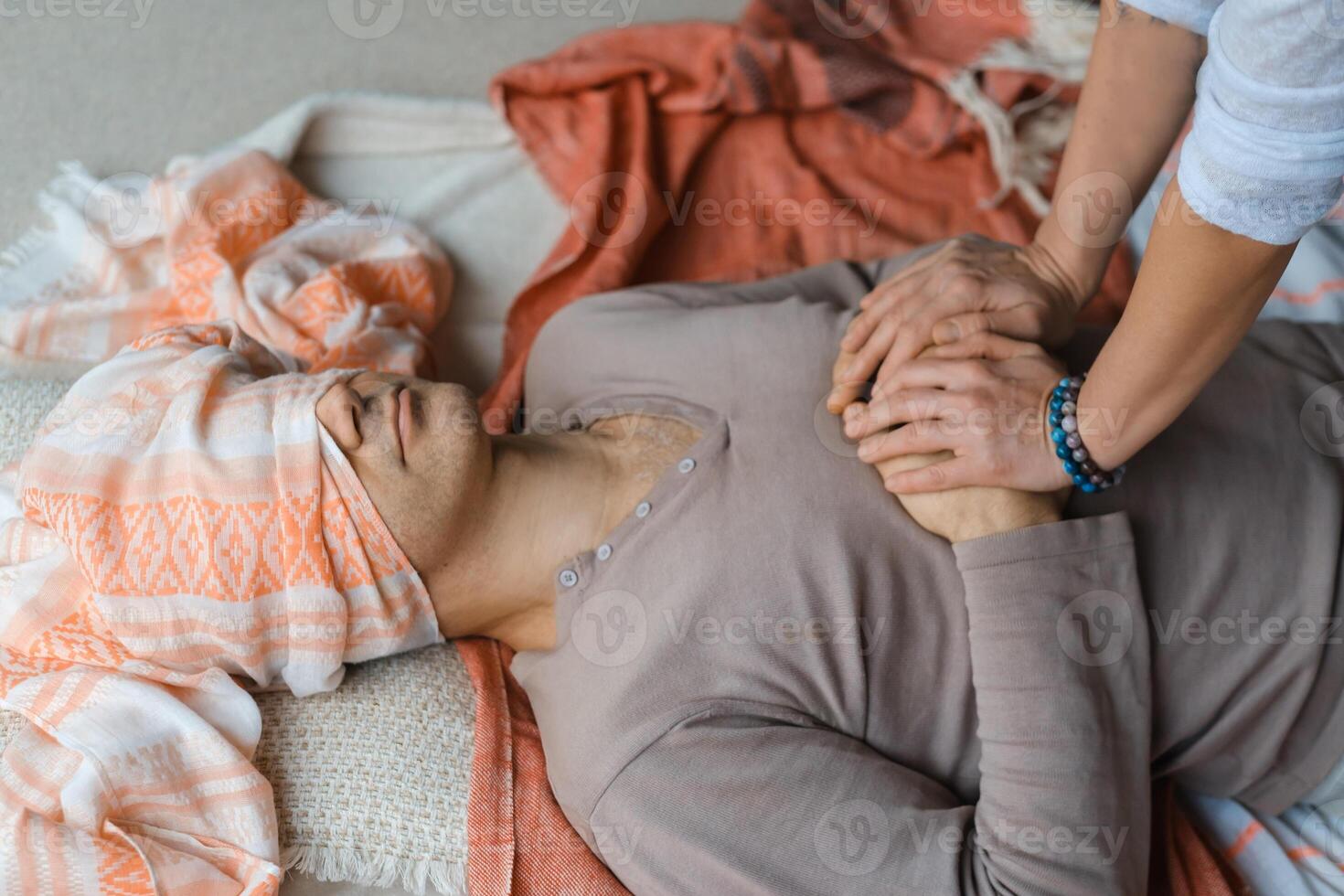 Man lying on the floor while a person ties a cloth around his eyes during a relaxation or meditation practice in a serene indoor setting... photo