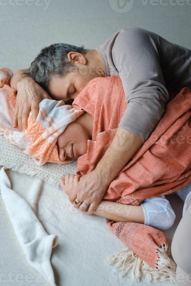 Couple embracing each other intimately while bundled in cozy blankets on a soft floor during a serene moment at home in the afternoon photo