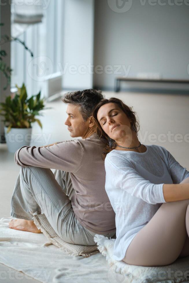 Couple engaging in mindfulness meditation practice while seated back to back in a serene indoor space during the late afternoon light.. photo