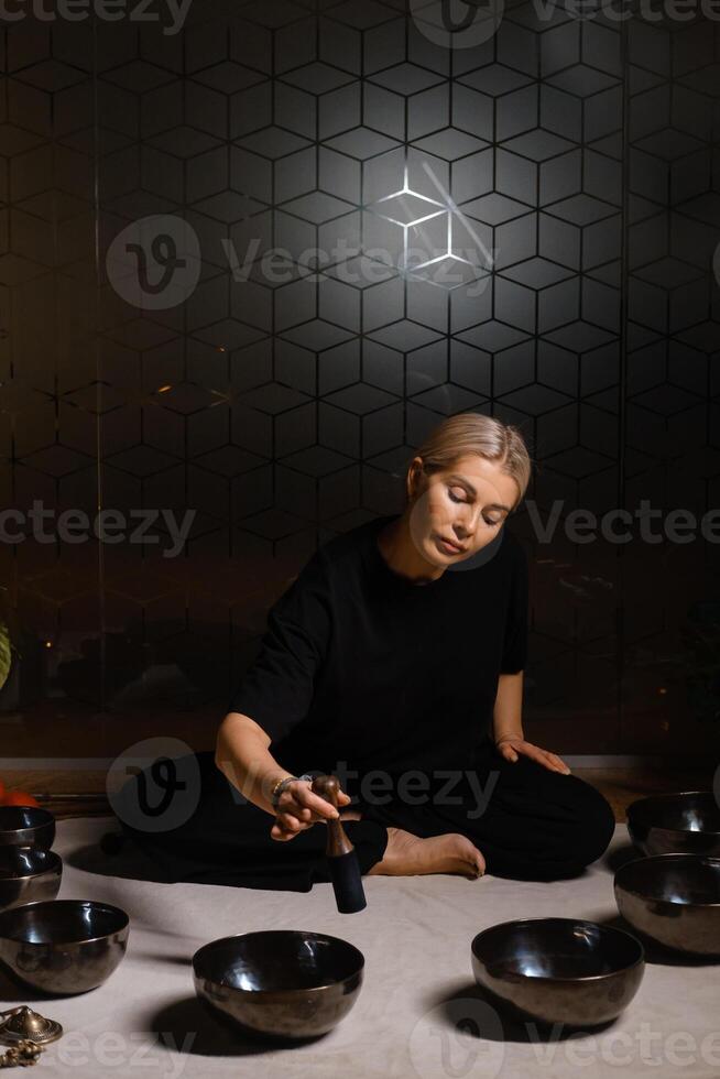 Woman practicing sound healing with singing bowls in a tranquil indoor space decorated with plants and soft lighting during a peaceful evening session.... photo