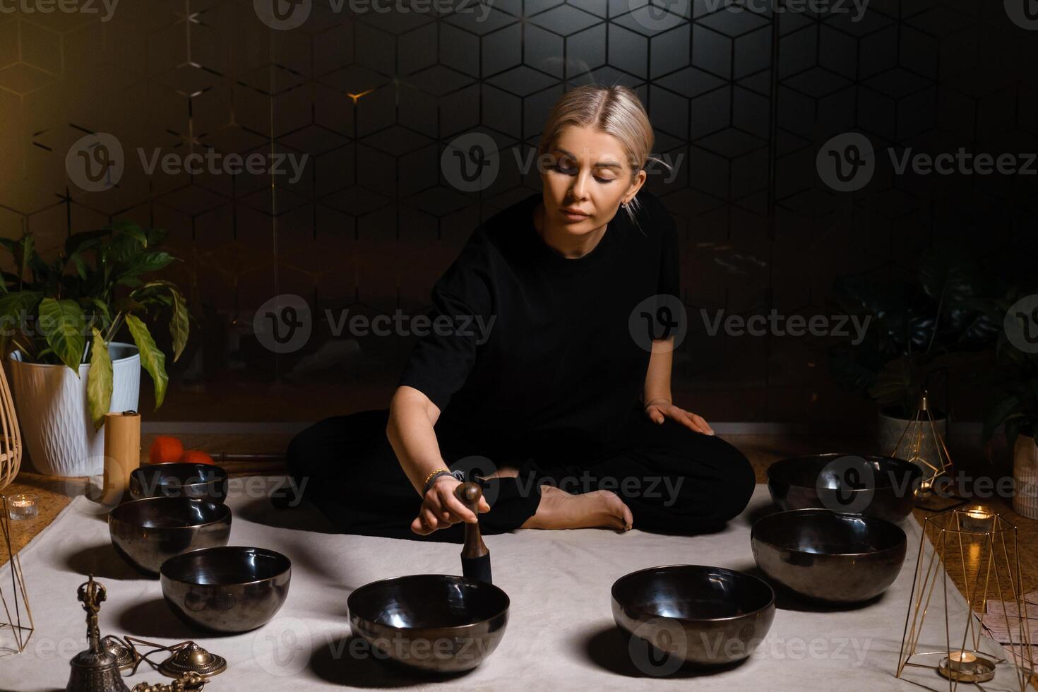 Woman practicing sound healing with singing bowls in a tranquil indoor space decorated with plants and soft lighting during a peaceful evening session.. photo
