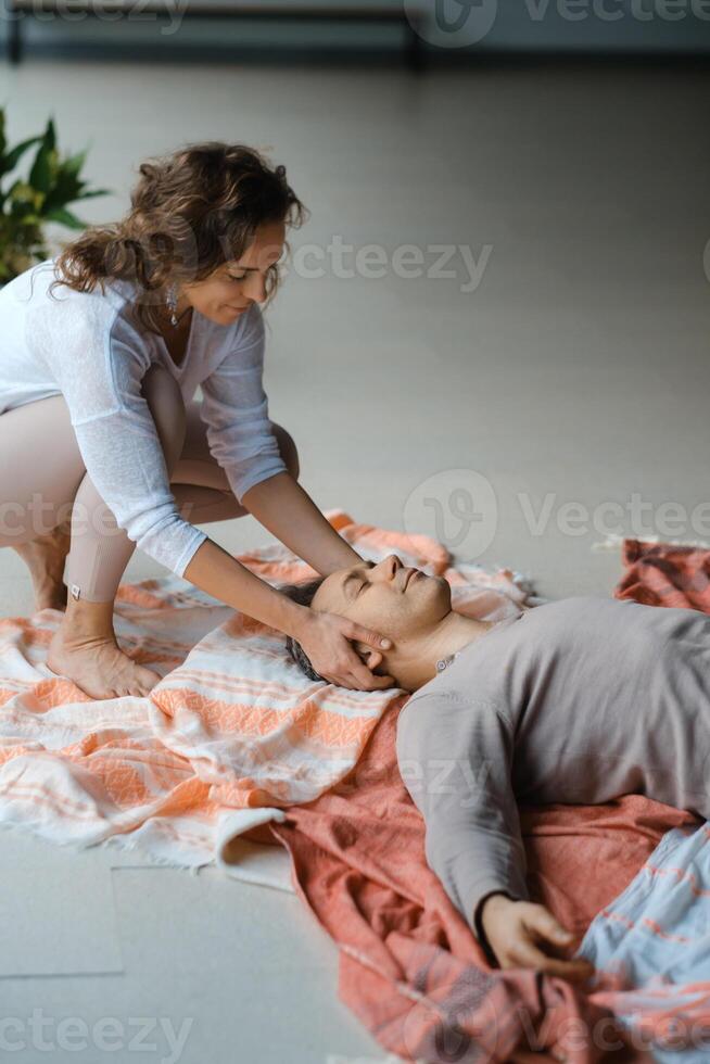 Man lying on the floor while a person ties a cloth around his eyes during a relaxation or meditation practice in a serene indoor setting.. photo