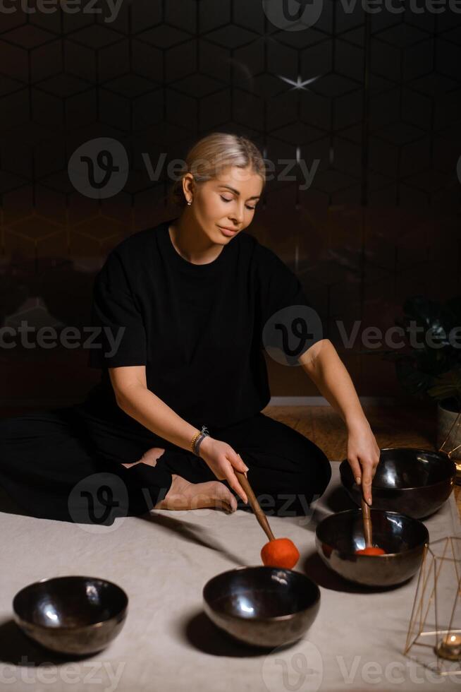 Woman practicing sound healing with singing bowls in a tranquil indoor space decorated with plants and soft lighting during a peaceful evening session... photo