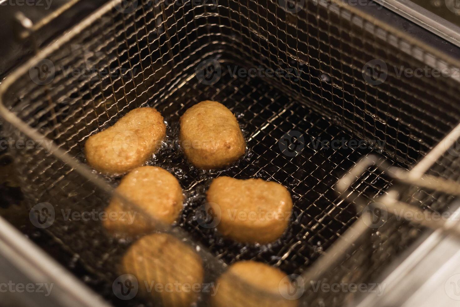 Golden brown chicken nuggets frying in hot oil in a kitchen setting during lunchtime, showcasing a tasty snack preparation photo