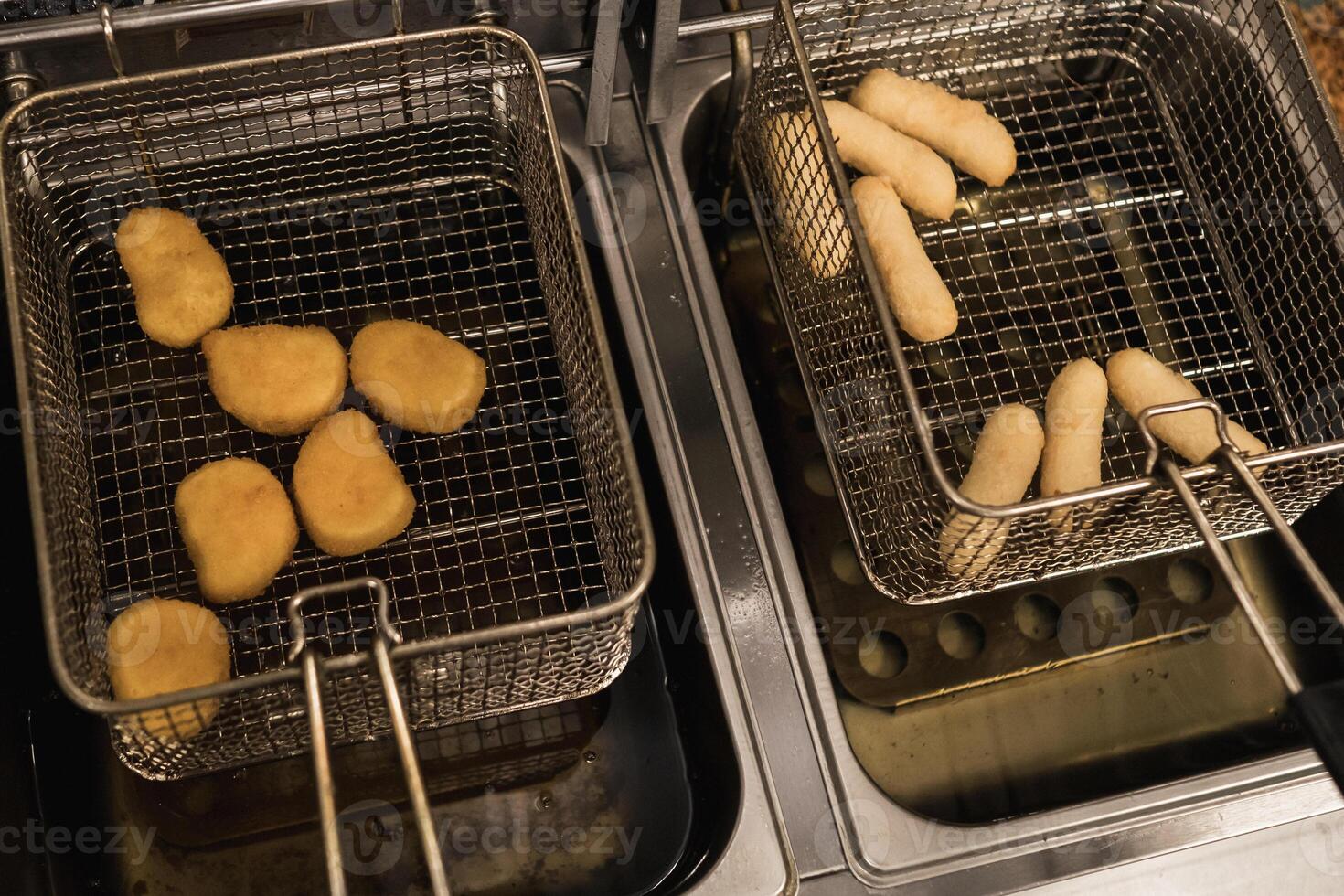 Fried snacks cooking in deep fryer with various shapes and sizes being prepared in a restaurant kitchen during busy afternoon hours photo