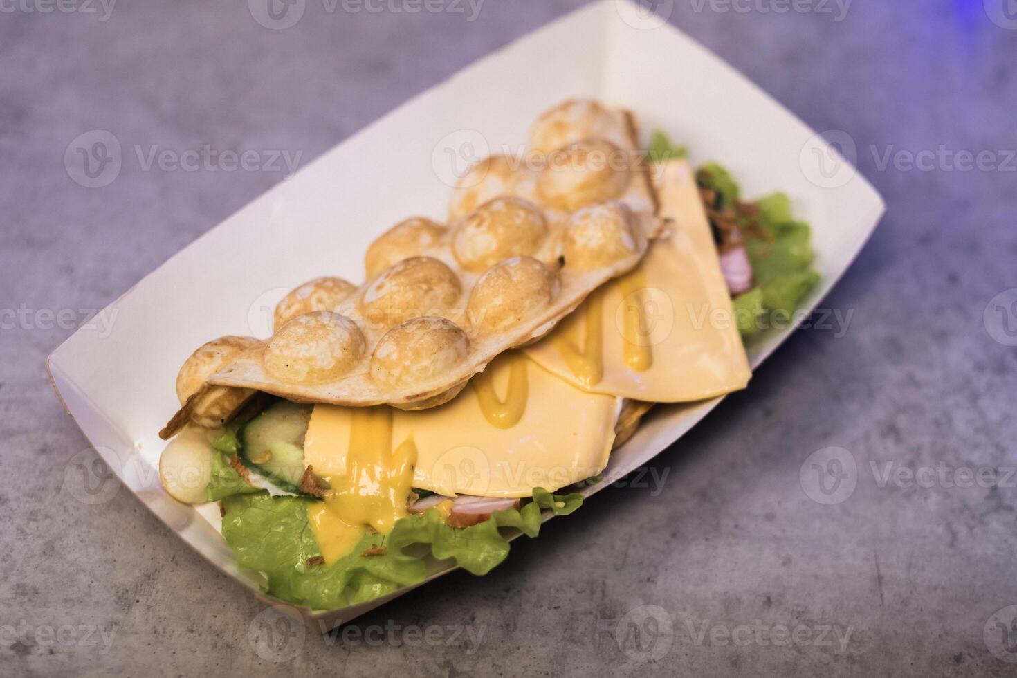 Delicious street food featuring a unique combination of fluffy egg waffles, fresh vegetables, and melted cheese served in a vibrant food stall photo