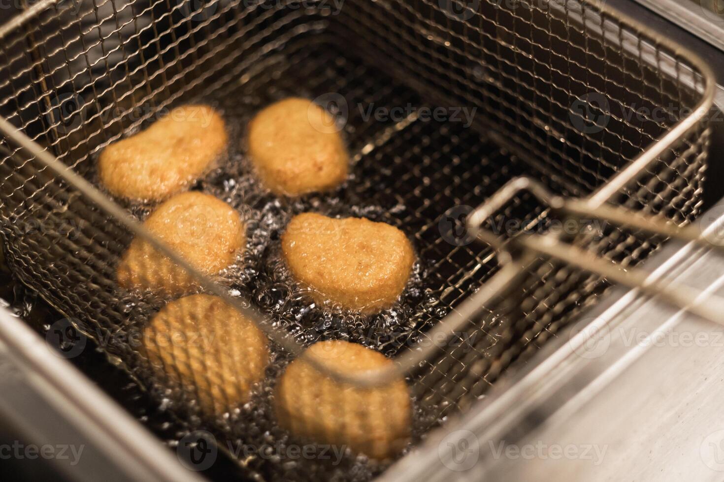 Golden brown chicken nuggets frying in hot oil in a kitchen setting during lunchtime, showcasing a tasty snack preparation. photo