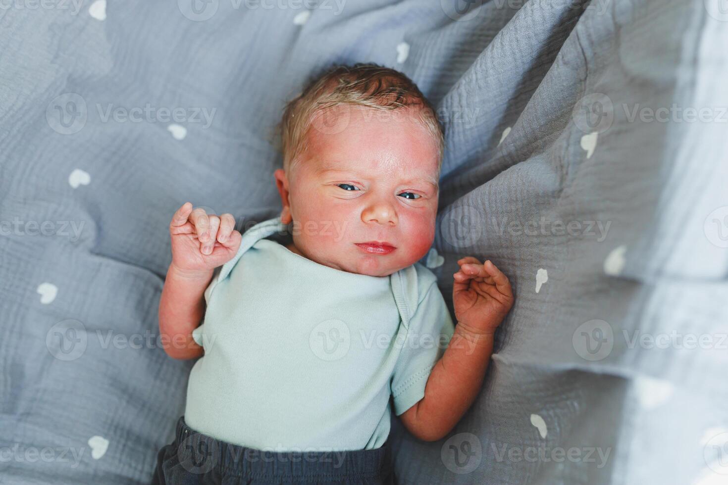 An adorable newborn baby is lying comfortably on a soft, cozy gray blanket adorned with heart patterns, beautifully captured in soft, natural light that enhances the scenes warmth and tenderness photo