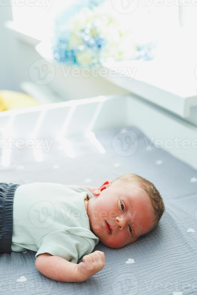 An adorable little baby is seen relaxing peacefully on a soft gray mattress positioned near a window, with beautiful natural light gently streaming in, creating a serene and warm atmosphere photo
