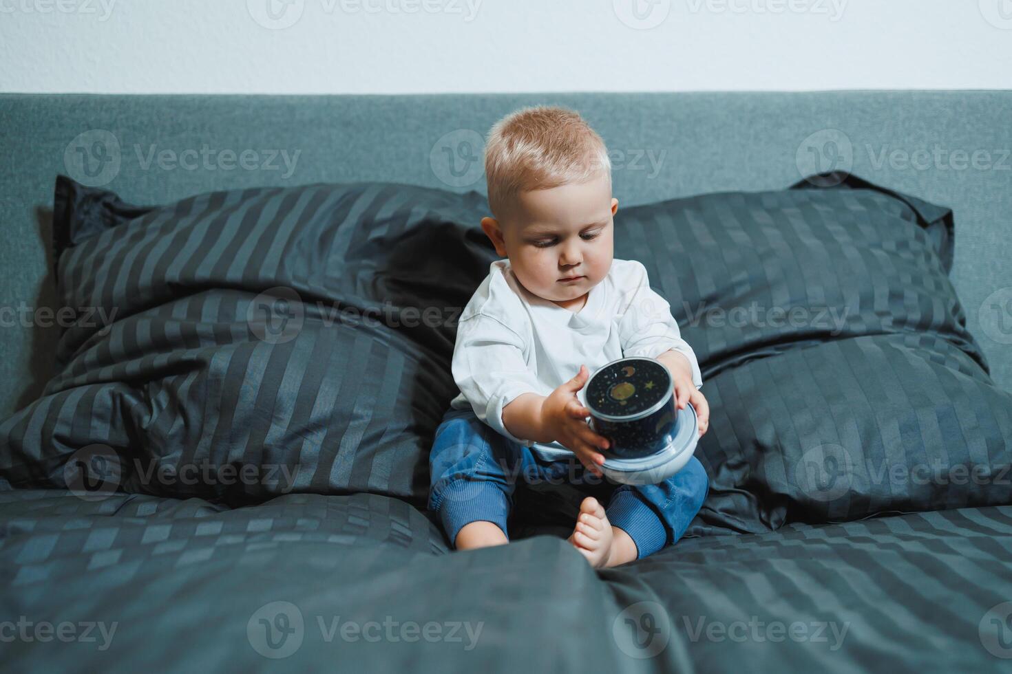 A joyful and happy toddler is happily and energetically playing with a colorful container on a cozy, warm bed surrounded by soft, fluffy pillows, showcasing the pure joy and wonder of early childhood photo
