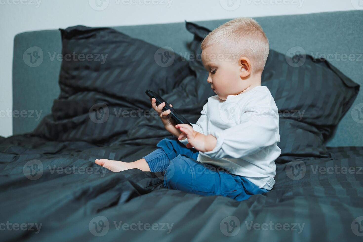 A toddler is comfortably engaged with a smartphone while nestled in a cozy bed, showcasing a blend of innocence, curiosity, and the interaction between childhood and modern technology photo