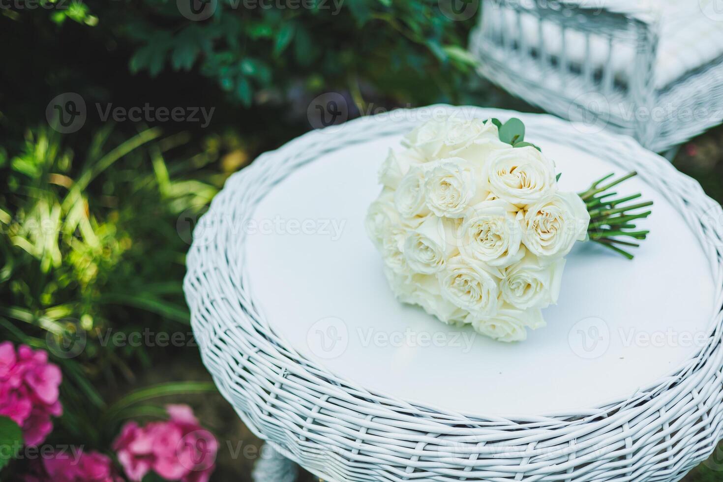 An Elegant White Rose Bouquet Arranged on a Wicker Table Set Within a Beautiful Garden Setting photo