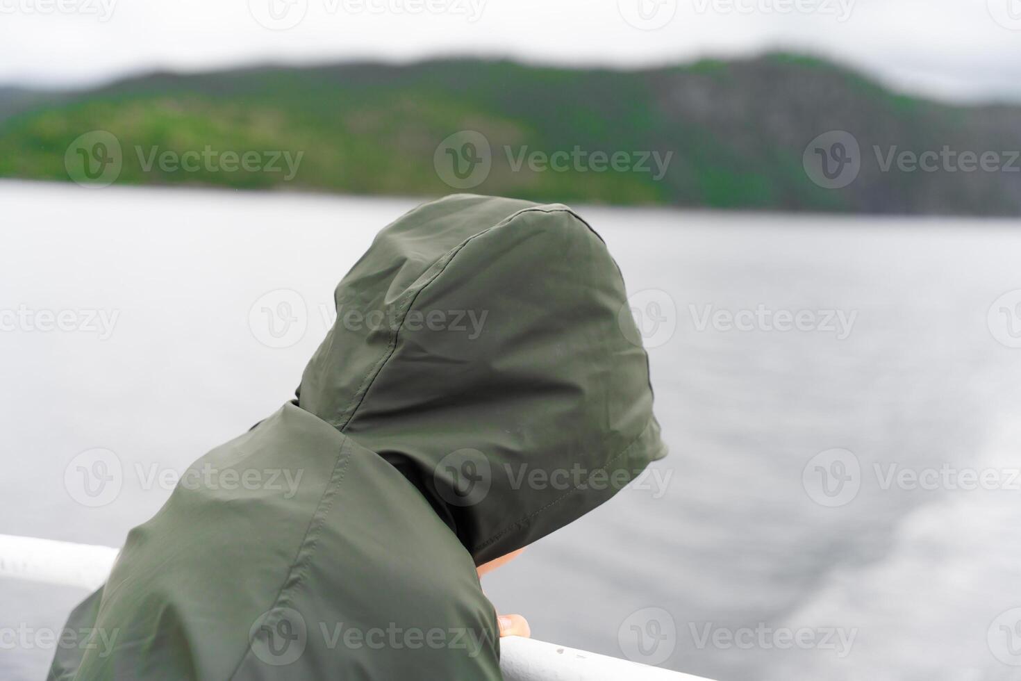 Child in green raincoat looking at water from ferry deck in Norway photo