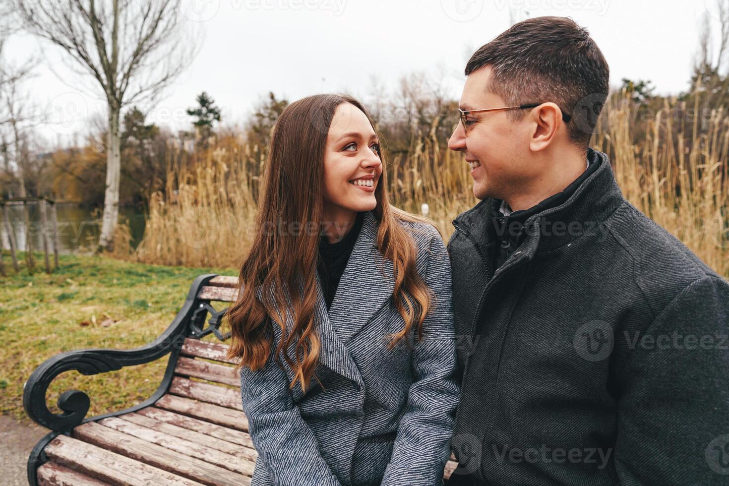 Couple enjoying a cozy moment on a park bench during an overcast autumn day by the lake photo