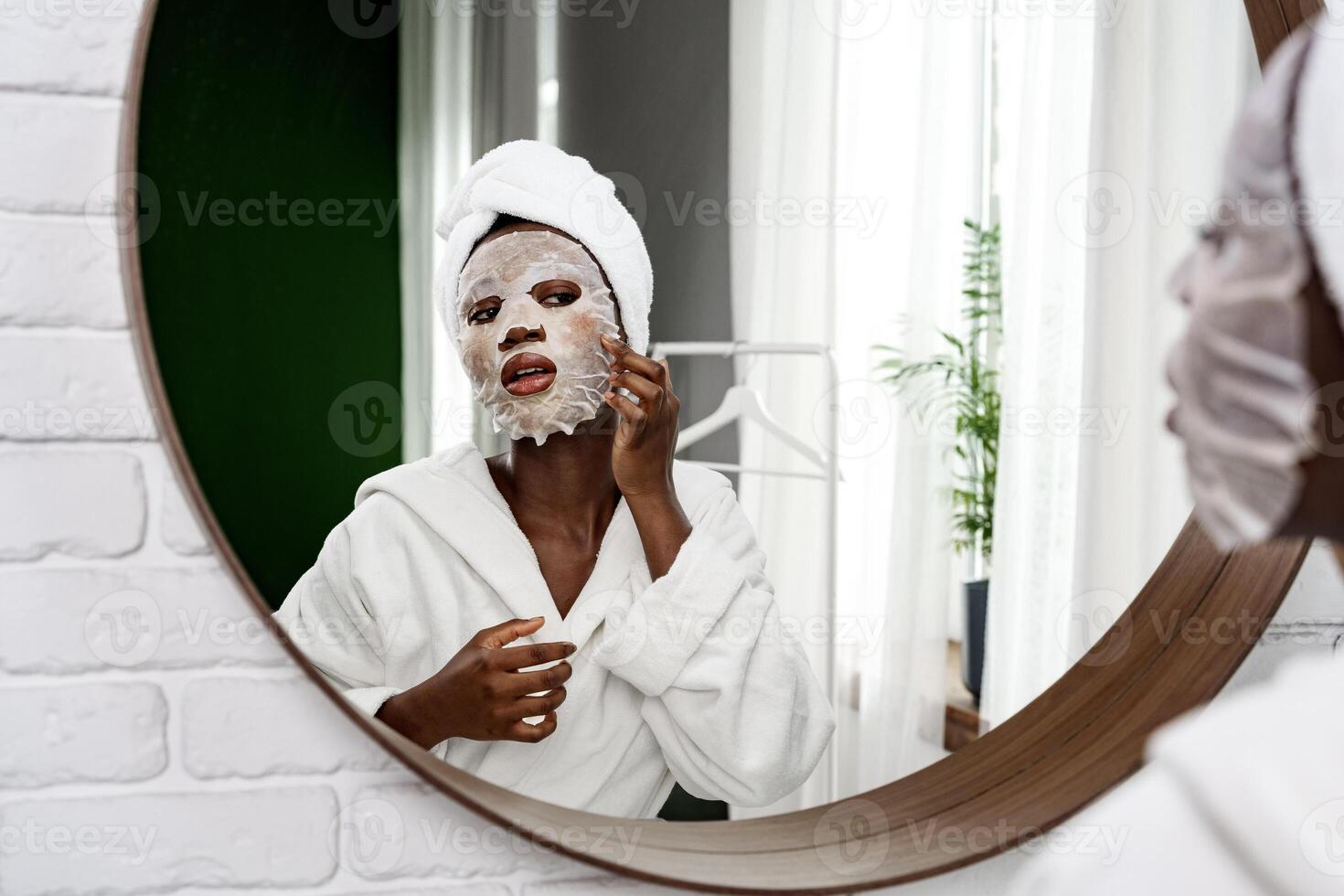 Self-care routine in a bright bathroom with a woman applying a facial mask and wearing a robe photo