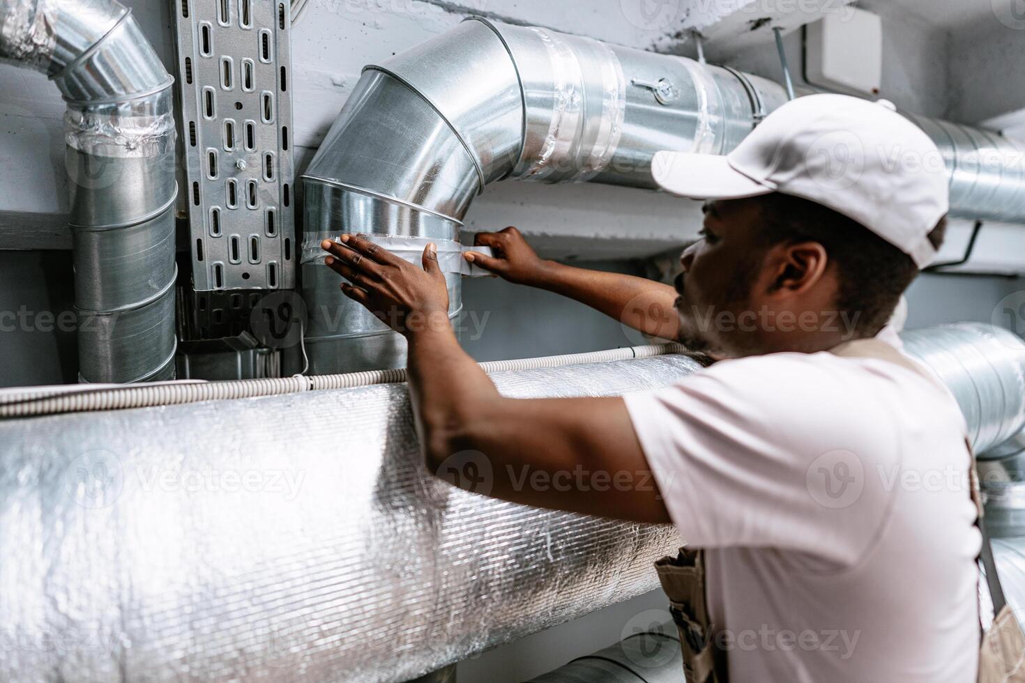 Skilled technician performing maintenance on metal air duct system in a commercial building workshop photo