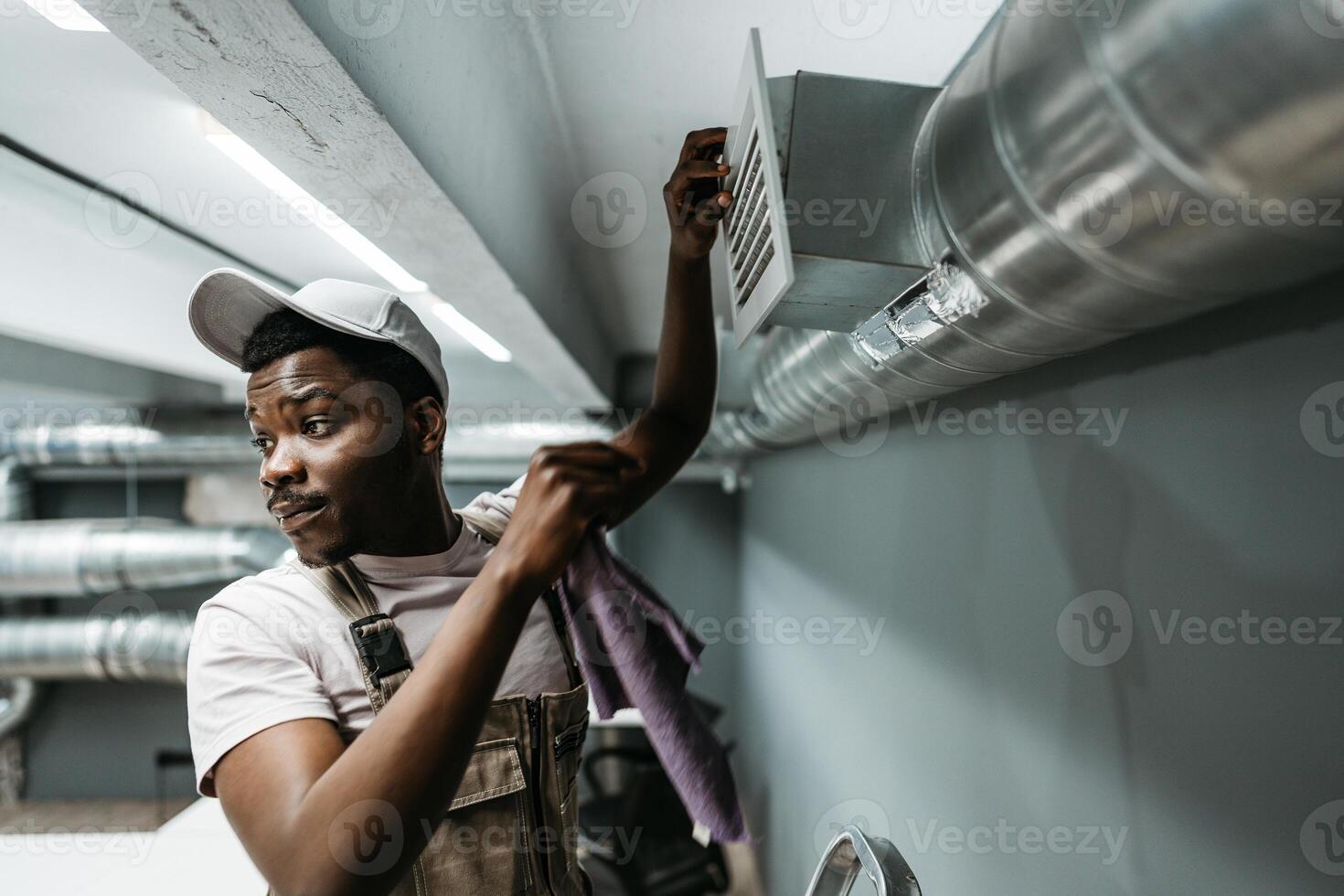 Worker performs maintenance on ventilation system in commercial building during daytime hours photo