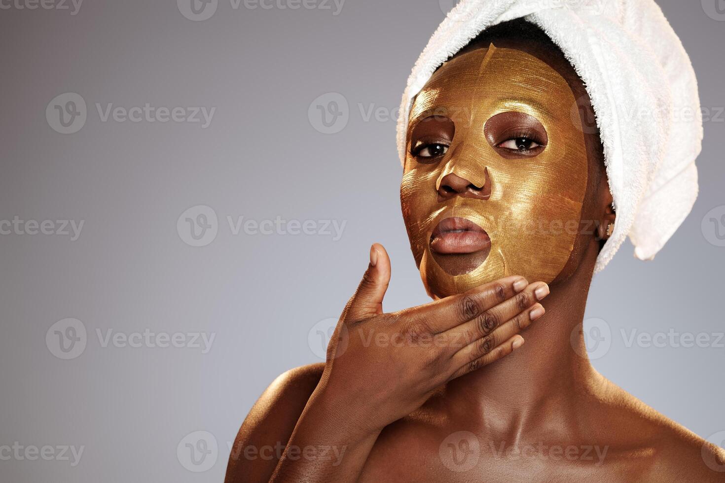 Woman applying a gold facial mask while wrapped in a towel showcasing skincare routines in a clean indoor setting photo