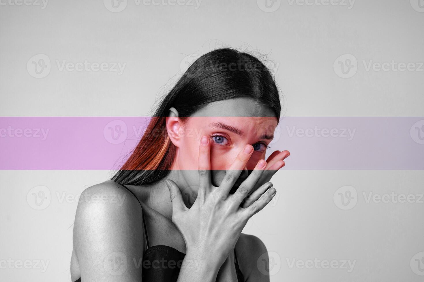Young woman expressing emotions with hands covering her face in a stylized monochrome and colored setting photo