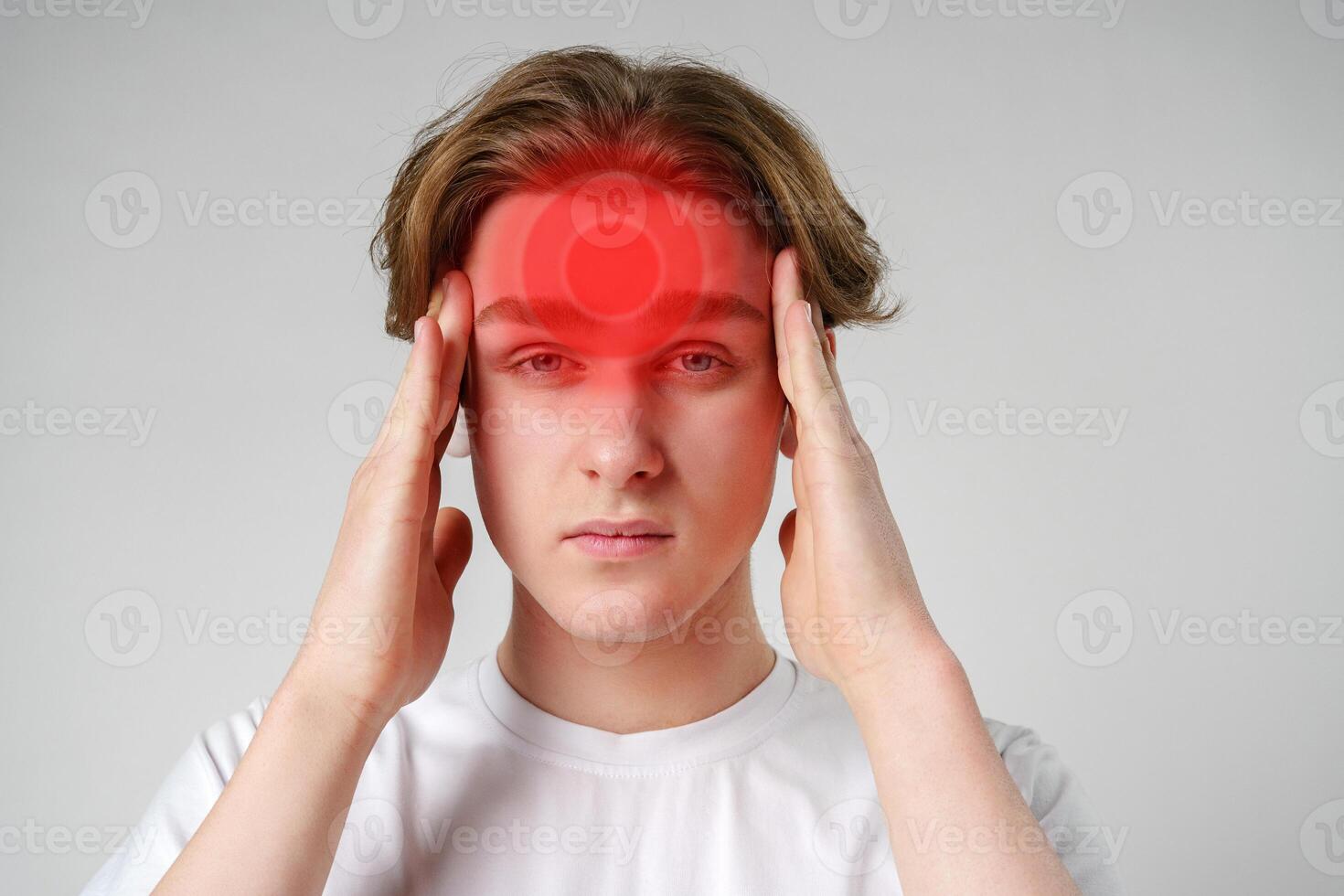 Young man experiencing headache in a minimal background setting while holding his forehead in discomfort photo