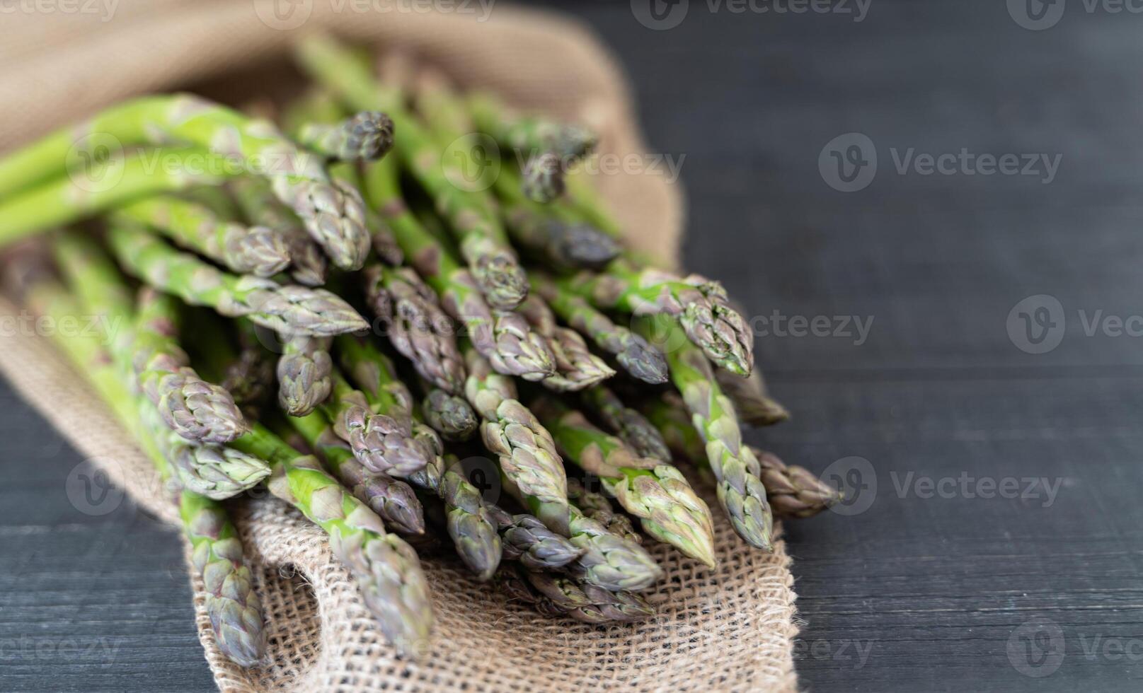 A bundle of green asparagus on a dark wood surface with coarse sackcloth, evoking a farm-fresh feel. photo