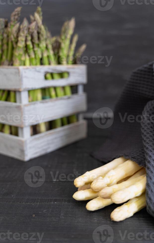 Gray crate with fresh green asparagus stems in background and white bundle in front photo