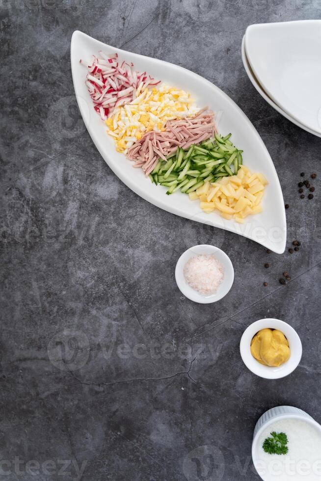 A rustic yet modern okroshka prep setup featuring fresh ingredients and condiments on a deep gray surface. photo