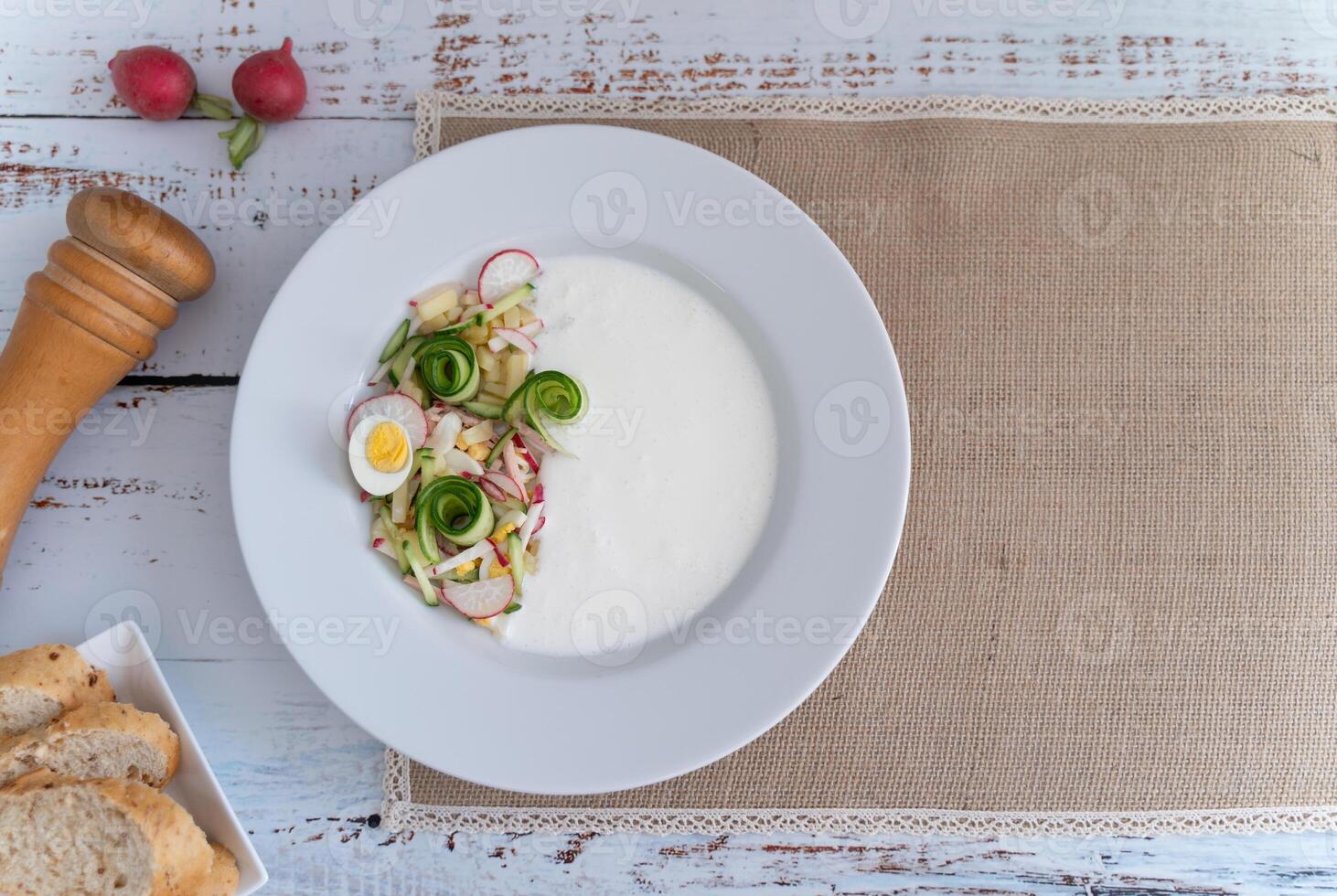 A rustic yet modern okroshka prep setup featuring fresh ingredients and condiments in round dish photo