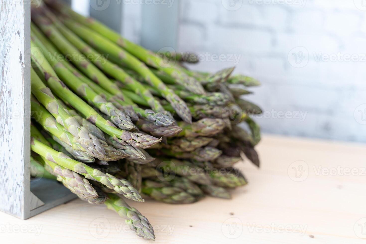 Crisp green asparagus spears falling out of a rustic gray wooden crate on a neutral background photo