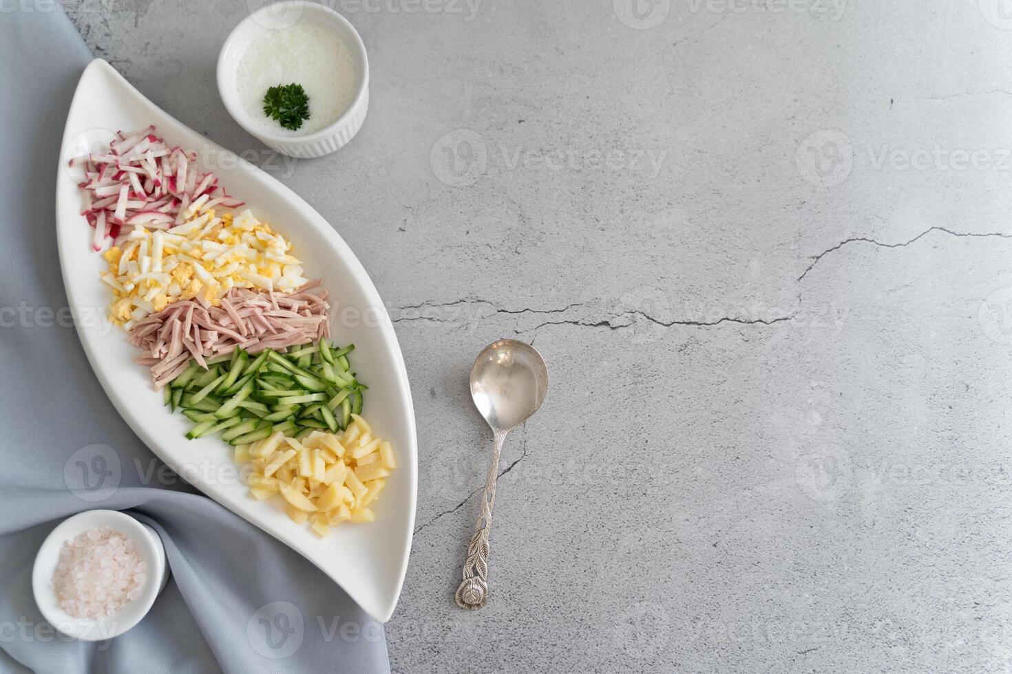 Elegant overhead view of okroshka prep with fresh ingredients and condiments placed on a light gray background. photo