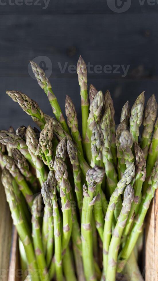 Top-down photo of green asparagus stalks arranged in a crate on a dark wooden surface for a farm-fresh feel