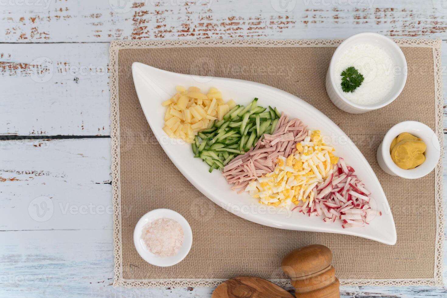 Okroshka ingredients displayed in a sleek white dish with condiment bowls on rustic cloth photo