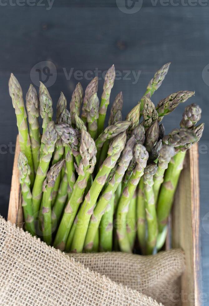 Top-down close-up of fresh green asparagus in a wooden crate, partially wrapped with rustic sackcloth photo