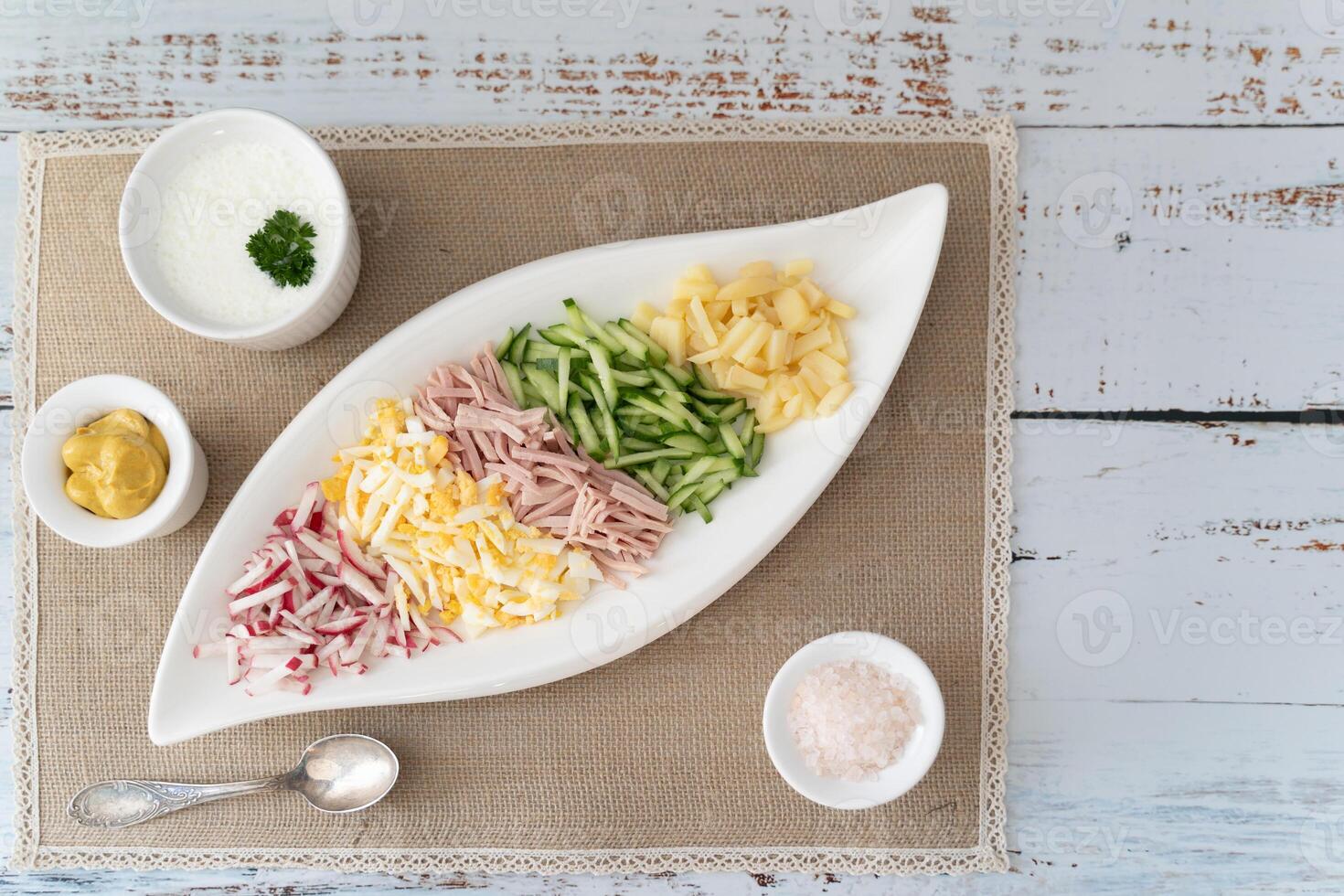 A flatlay of diced vegetables and herbs for okroshka, with kefir and mustard photo