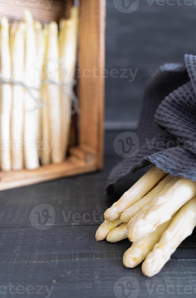 White asparagus against dark background, bundle in front and some stacked in wooden crate photo