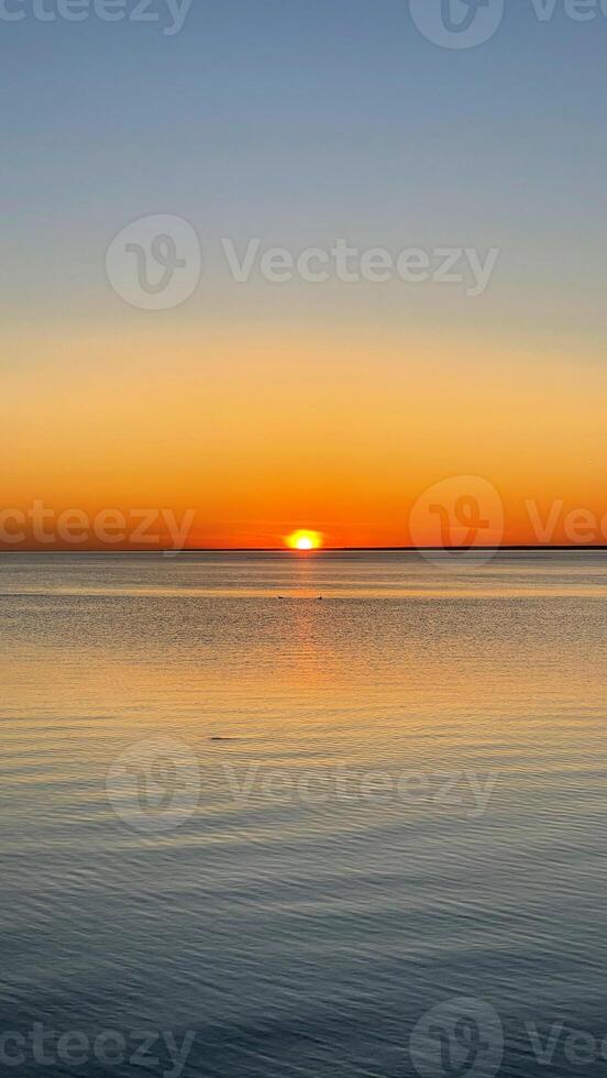 Beautiful sunset over the sea. The sun sets on the water. The sky is painted with bright colors. Summer evening. Sunset beach. Vertical photo