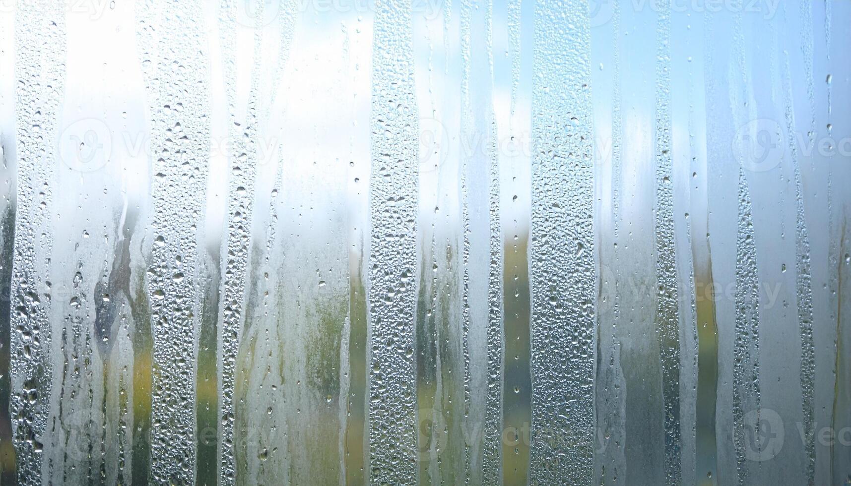 Water Droplets Create a Textured Pattern on a Glass Window With a Blurred Green Landscape Outside photo
