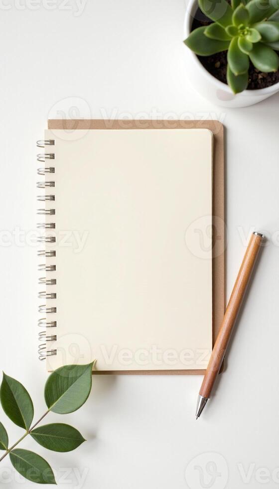 Minimalist workspace with brown notebook and pencil on white background and greenery. photo