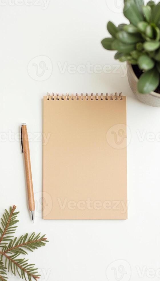 Flat lay of notebook and pencil with green leaves on white table. photo