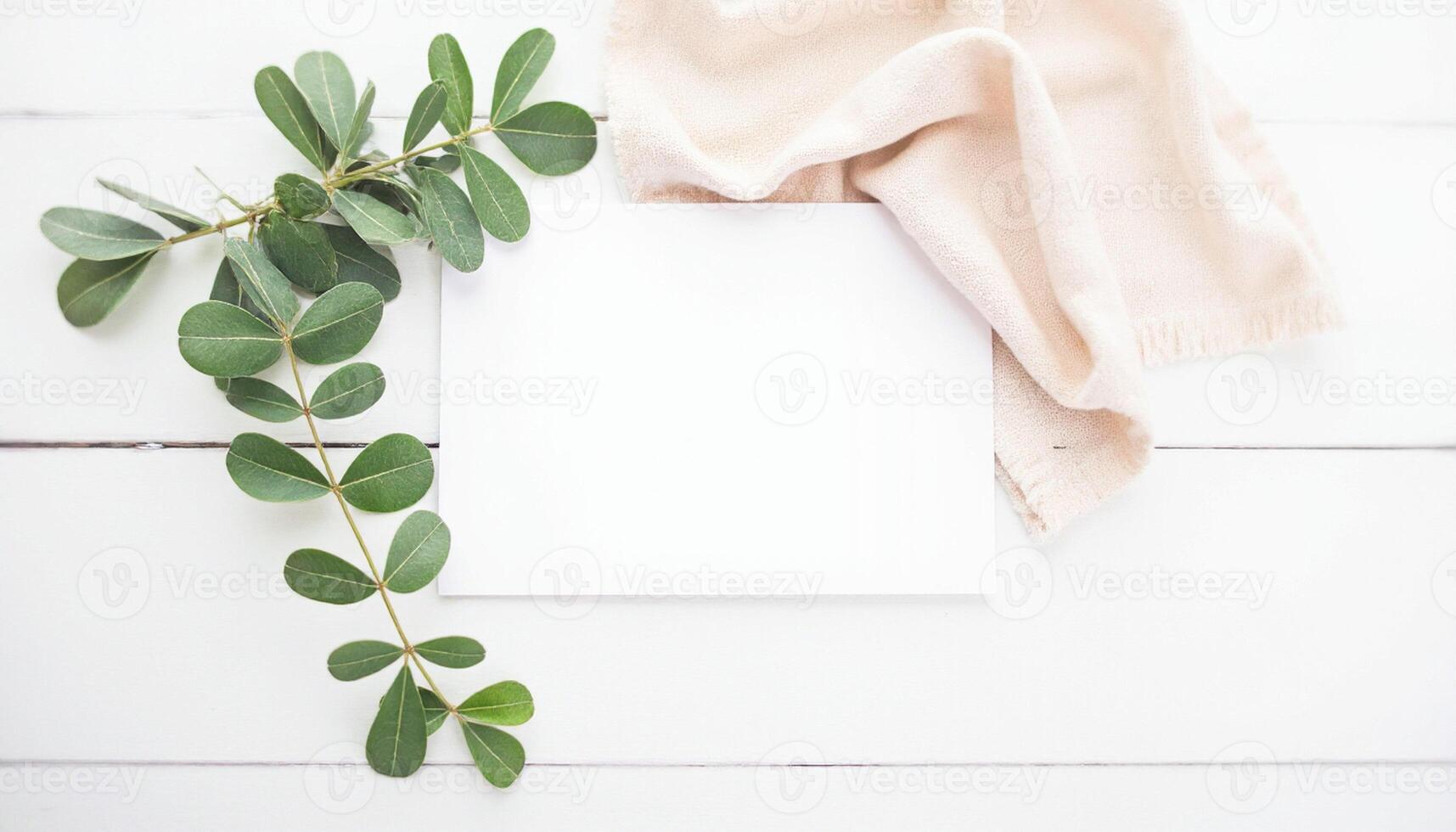Blank paper, eucalyptus leaves and a towel on a white wooden table top view photo