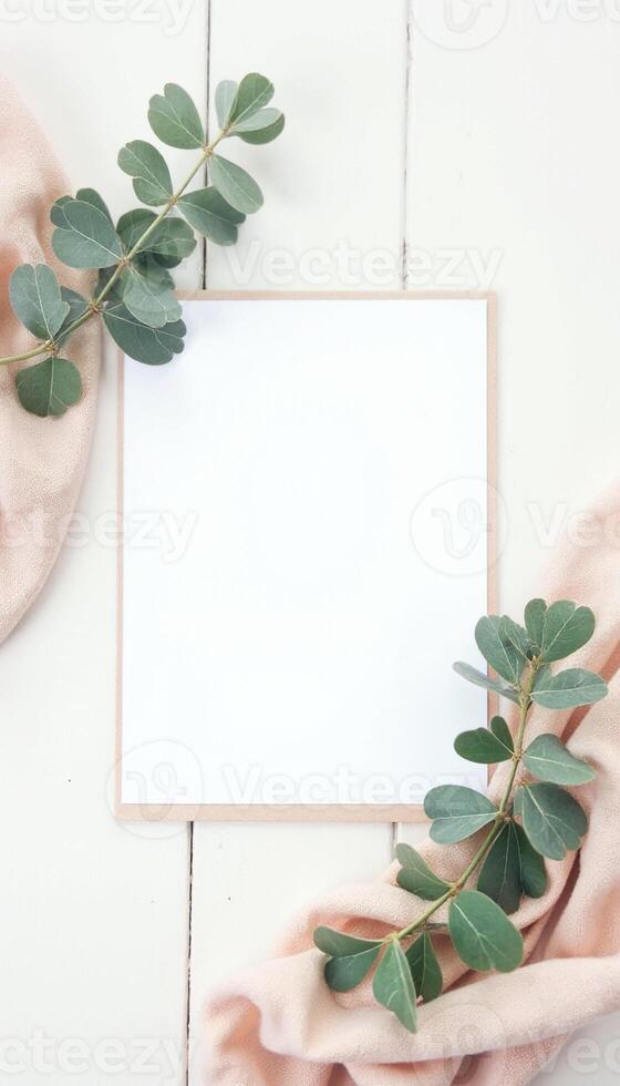 Blank white paper with eucalyptus leaves on a white wooden table top view photo