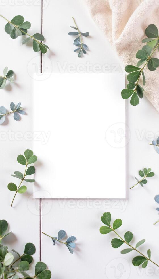 Blank white card with eucalyptus leaves on white table top view photo