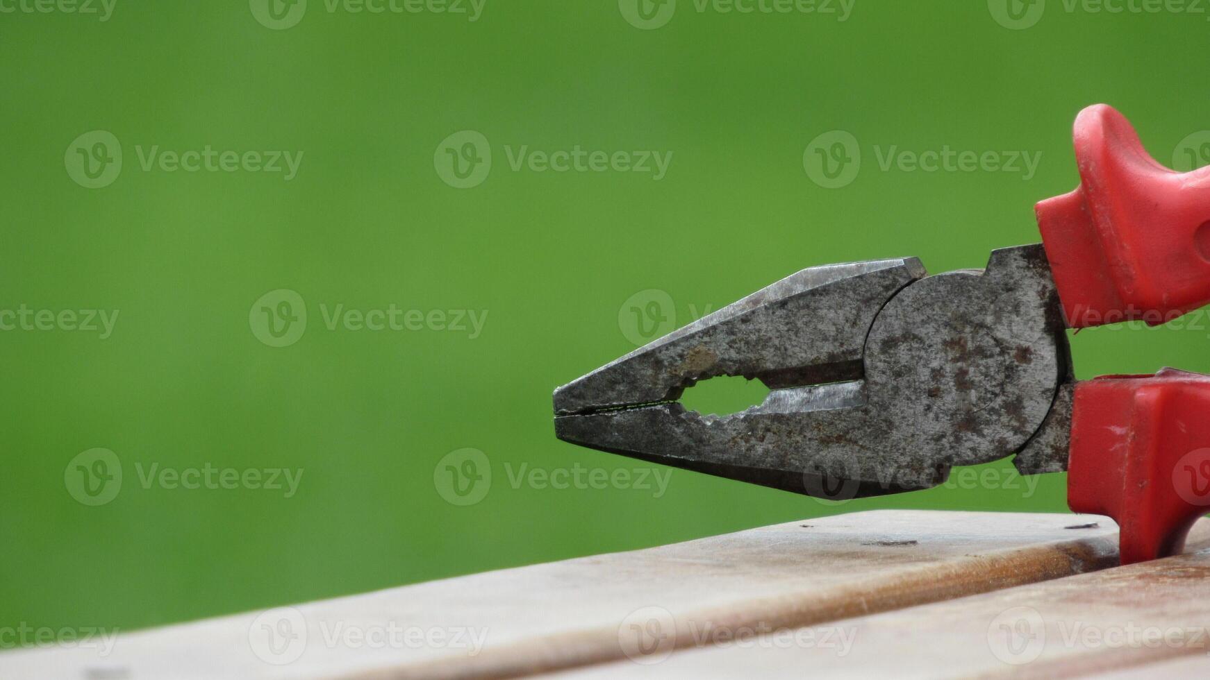 Pliers resting on a wooden surface in a green outdoor setting during daylight hours photo