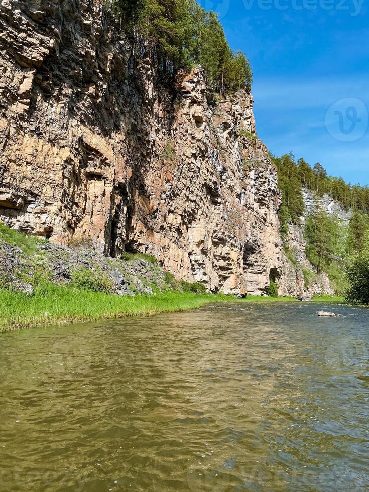 A beautiful and serene river is flowing gently through a stunning canyon, with a majestic cliff rising prominently in the background, creating a picturesque natural landscape photo