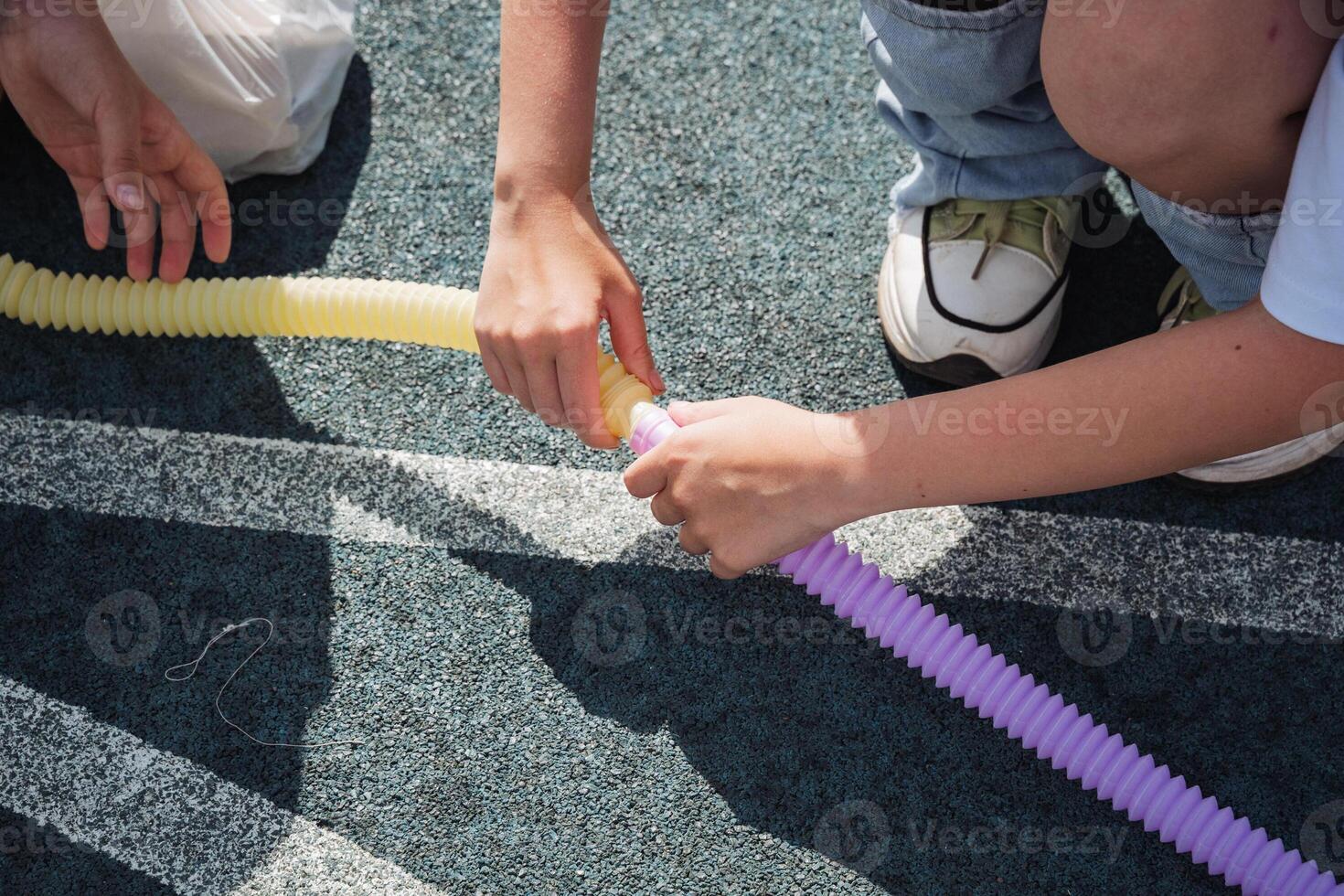 A person is joyfully playing with a long, bright yellow and purple inflatable tube, delighting in a sunny day spent outdoors, surrounded by a vibrant and cheerful atmosphere filled with laughter photo