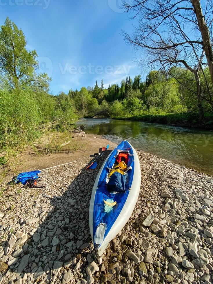 A vibrant blue and white kayak is currently resting on the rocky shore near a flowing river, creating a picturesque scene that captures the essence of outdoor adventure and recreation photo