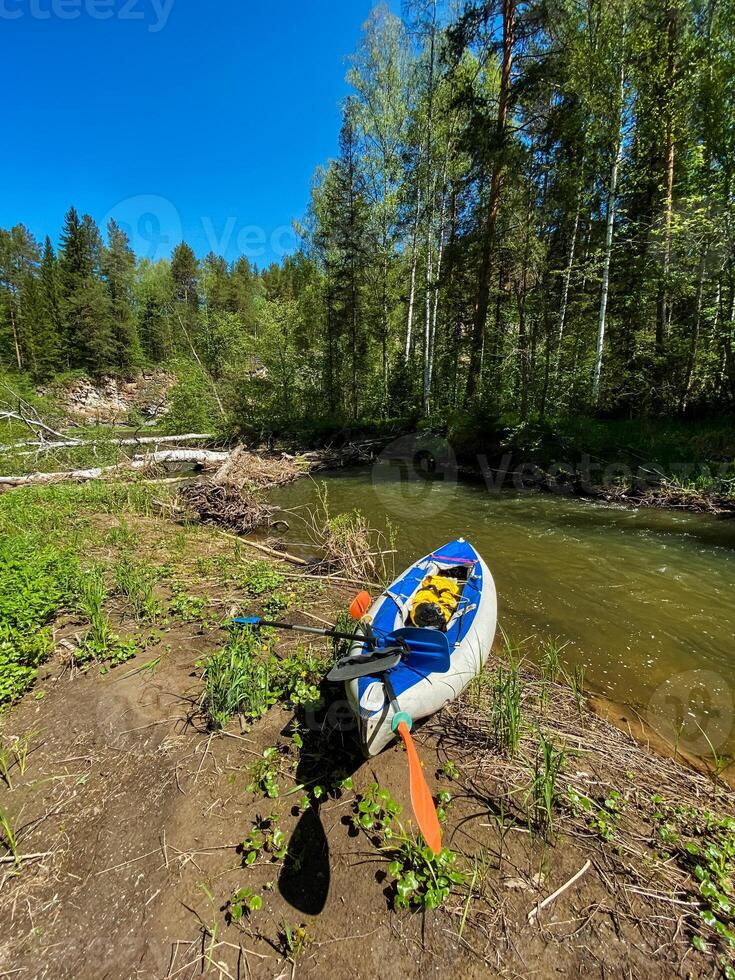 A bright and colorful kayak, complete with its sturdy paddle, is sitting quietly on the sandy shore of a gently flowing river, waiting patiently for its next adventure in the water photo