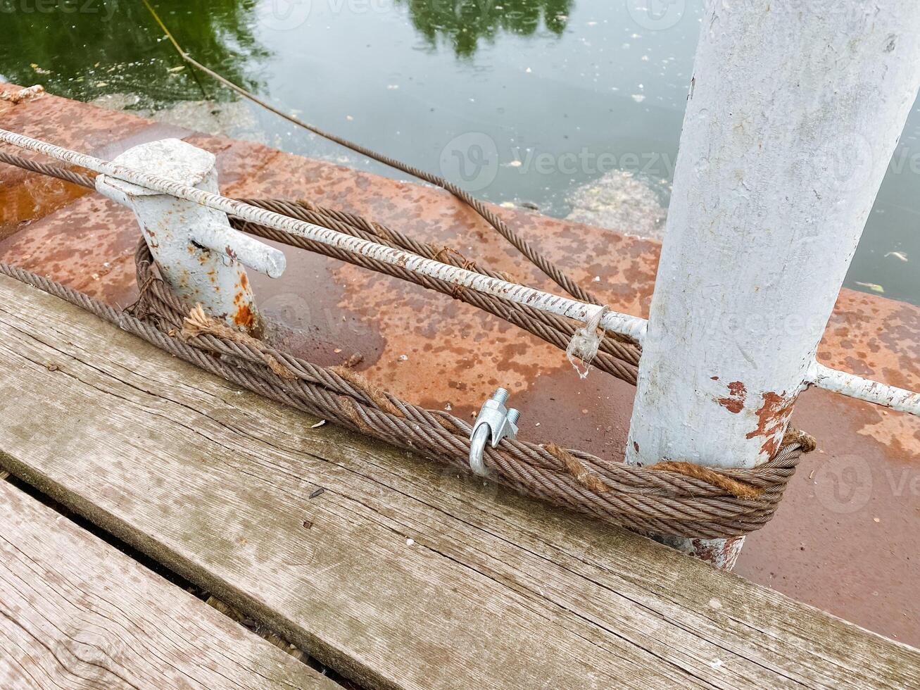 A weathered and rustic dock hardware piece featuring twisted rope laid upon aged wooden planks, capturing a sense of calm and tranquility in a serene coastal environment by the water photo