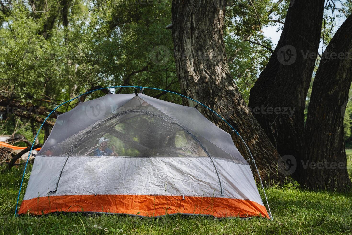 Imagine a cozy camping tent blissfully situated underneath a canopy of lush green trees, surrounded by the beauty and tranquility of nature, perfect for an adventurous getaway amidst the wilderness photo